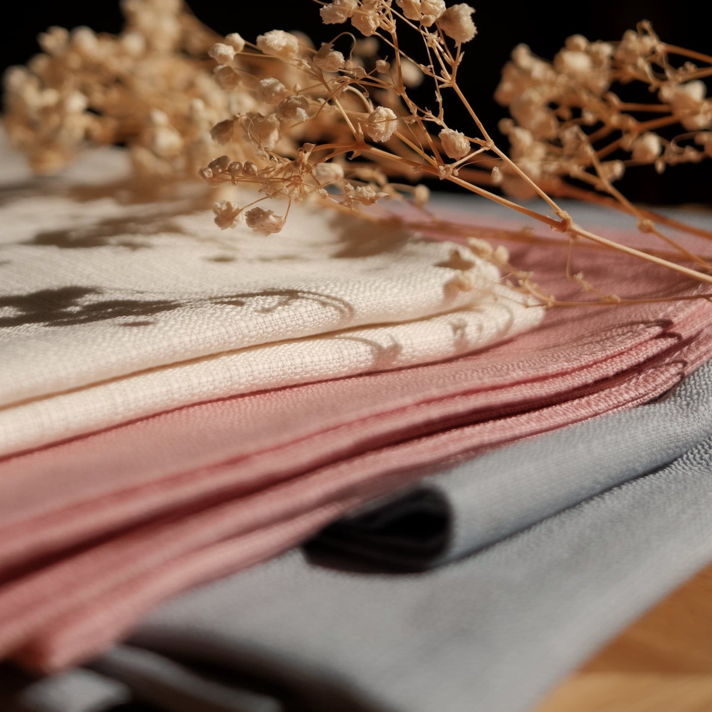 Stack of pink, white and blue furoshiki fabric with dried flowers on a textured surface