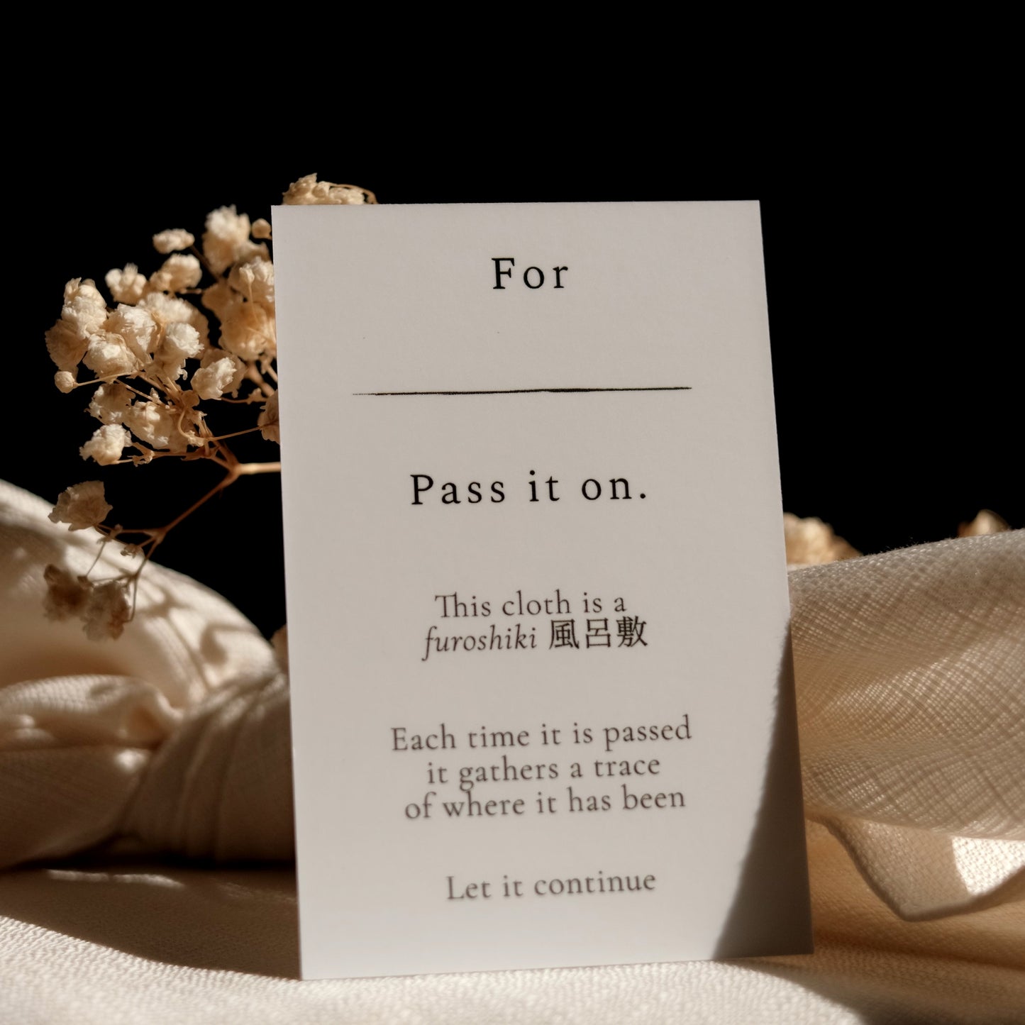 White card with text about a furoshiki cloth and dried flowers on a dark background