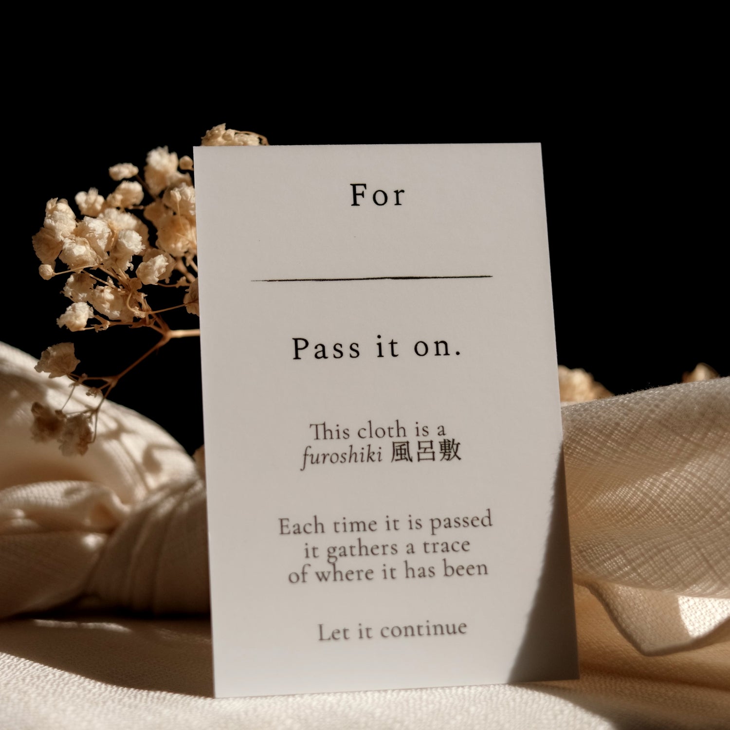 White card with text about a furoshiki cloth and dried flowers on a dark background